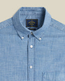 Chemise Chambray Bleue Portuguese Flannel, col boutonné, détails des boutons blancs et étiquette de marque.