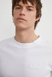 T-shirt Essentiel Hortensia Blanc LATER avec logo brodé, porté par un homme, gros plan.
