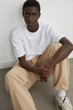 Homme portant le T-shirt Essentiel Hortensia Blanc de LATER..., assis avec un pantalon beige et des baskets.