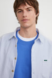 Homme portant la Surchemise ÉPURE Marine rayée bleu clair, ouverte sur un pull bleu vif.