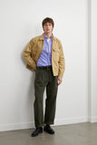 Blouson Worker beige LATER... porté par un homme avec une chemise rayée bleue et rose, un pantalon vert foncé et des chaussures noires.