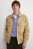 Blouson Worker Beige LATER... pour homme avec poches à rabat, porté sur une chemise rayée bleu et rose et pantalon vert foncé.