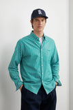 Chemise HEOL Rayures Vertes | LATER... portée par un homme. Chemise boutonnée rayée vert et blanc, pantalon sombre, casquette.