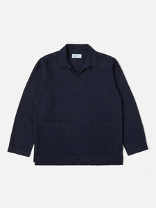 Smock Overshirt Indigo Herringbone Denim Universal Works, veste-chemise inspirée du workwear avec une coupe ample et confortable. Confectionnée en denim à chevrons indigo pour une texture subtile et un look authentique. Disponible exclusivement en boutique chez SEE YOU, concept store à Versailles.
