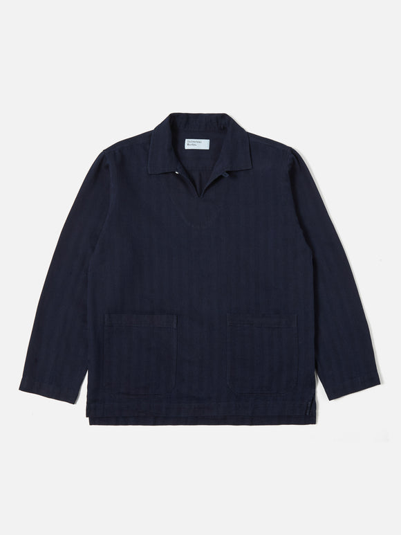 Smock Overshirt Indigo Herringbone Denim Universal Works, veste-chemise inspirée du workwear avec une coupe ample et confortable. Confectionnée en denim à chevrons indigo pour une texture subtile et un look authentique. Disponible exclusivement en boutique chez SEE YOU, concept store à Versailles.