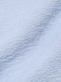 Gros plan sur le tissu seersucker de la L/S Utility Shirt Pale Blue Seersucker Universal Works. Texture légèrement gaufrée offrant légèreté et ventilation, idéale pour les saisons douces. À découvrir en boutique chez SEE YOU à Versailles.