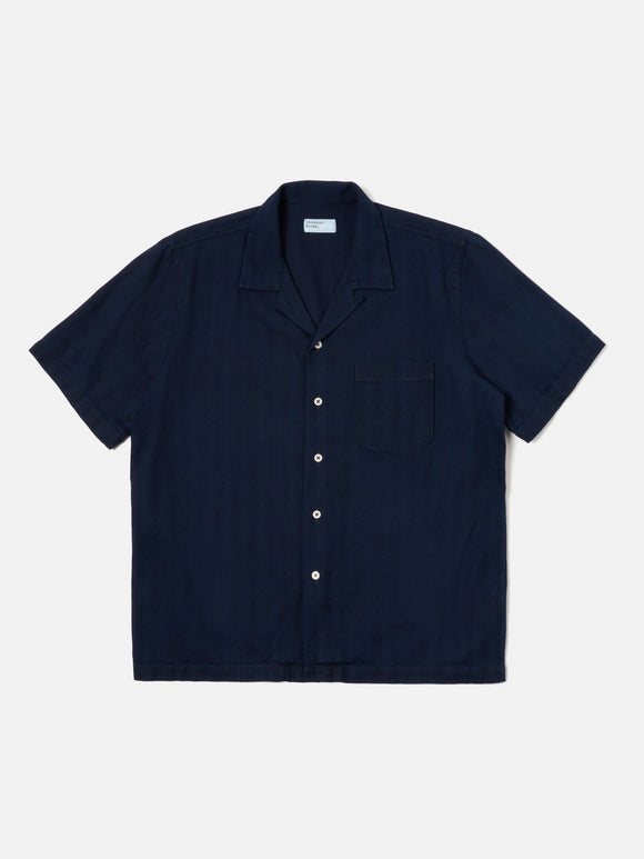 Road Shirt Indigo Herringbone Denim Universal Works, chemise en denim à chevrons avec une coupe droite et un col ouvert. Teinte indigo profonde pour un look intemporel et authentique. Disponible dans notre concept store homme à Versailles.
