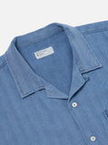 Détail du col ouvert et de la patte de boutonnage de la Road Shirt Washed Indigo Herringbone Denim Universal Works. Finitions minimalistes et boutons discrets pour une touche raffinée. Disponible en exclusivité dans notre concept store à Versailles.