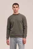 Homme portant le pull Danny 6429 Vert Kaki de NN.07, un pull texturé à manches longues avec un col rond, associé à un jean clair.