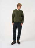 Cardigan en laine polaire Universal Works olive pour homme, porté avec une chemise claire, un pantalon noir et des baskets.