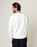 Homme de dos portant le Sweatshirt Aquae Ecru HOMECORE, avec coutures rouges sur le dos, et un pantalon foncé.