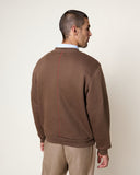 Homme de dos portant un Sweatshirt MKO Logo Cocoa HOMECORE marron avec une couture rouge verticale et un pantalon beige.