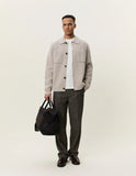 Homme portant une surchemise Maille Milano Light Sand Les Deux, un t-shirt blanc, un pantalon foncé et des mocassins, tenant un sac de voyage.