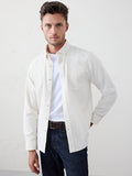 Homme portant une Chemise Velours Côtelé Fin Ivory Les Deux ouverte sur un t-shirt blanc, avec un jean et une ceinture marron.
