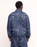 Veste Akka Life Dance Olow, veste en jean bleue avec des motifs abstraits blancs, portée par un homme de dos, pantalon similaire