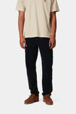 Pantalon Newel Carhartt WIP bleu marine foncé en velours côtelé porté par un homme avec un t-shirt beige et des chaussures bateaux marron.