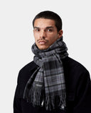 Homme portant une écharpe Carhartt WIP Parson Shady Purple à carreaux gris et violets avec franges, sur une veste noire.